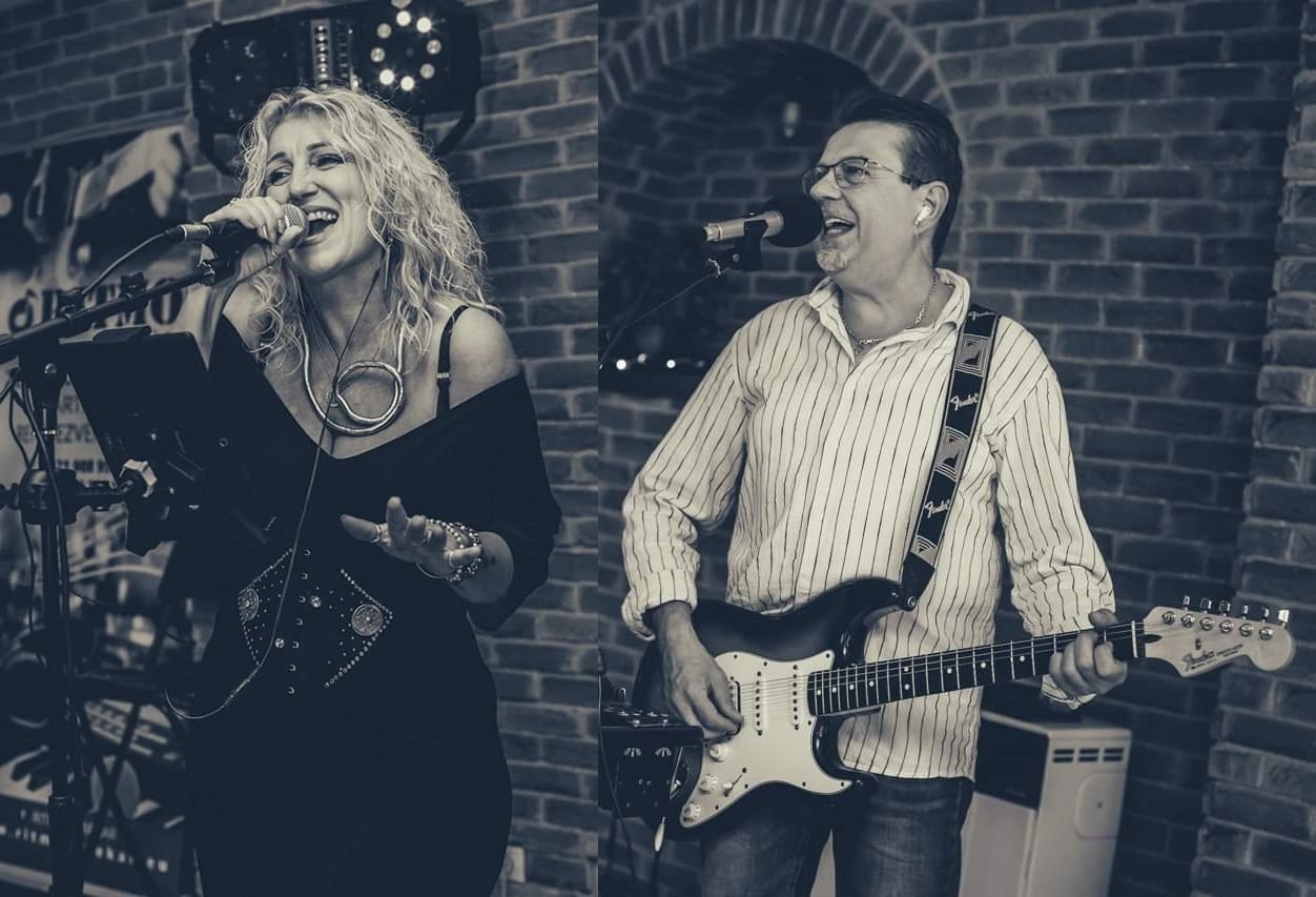 Gyurász Ildikó mikrofonnal énekel, mellette Leczkési Péter gitározik a RITMO zenekar egyik fellépésén